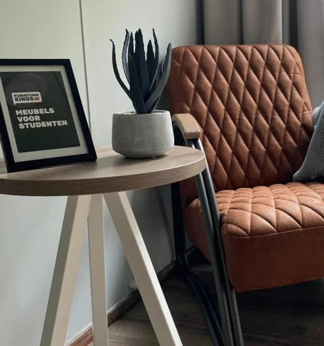 A chair and table in a room with a picture and plant on the table
