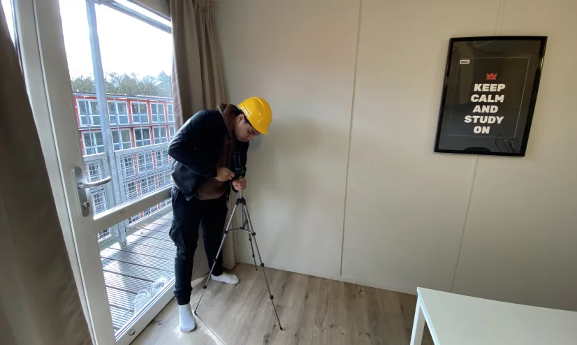 Man in yellow hard hat stands in front of window